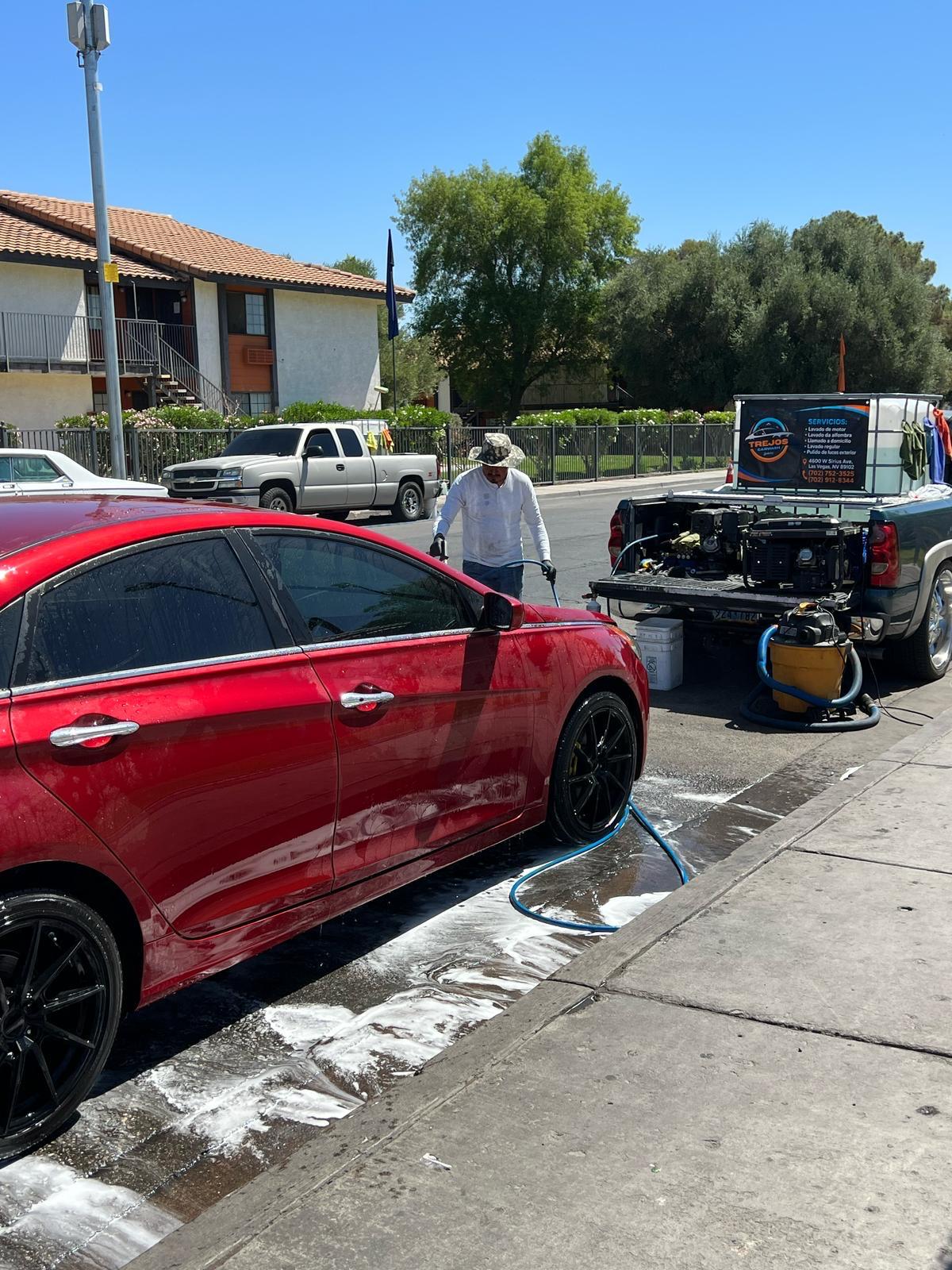 Detailer washing a red sedan with the mobile equipment truck in the background